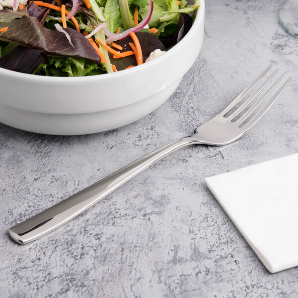 An Arcoroc stainless steel serving fork next to a bowl of salad.