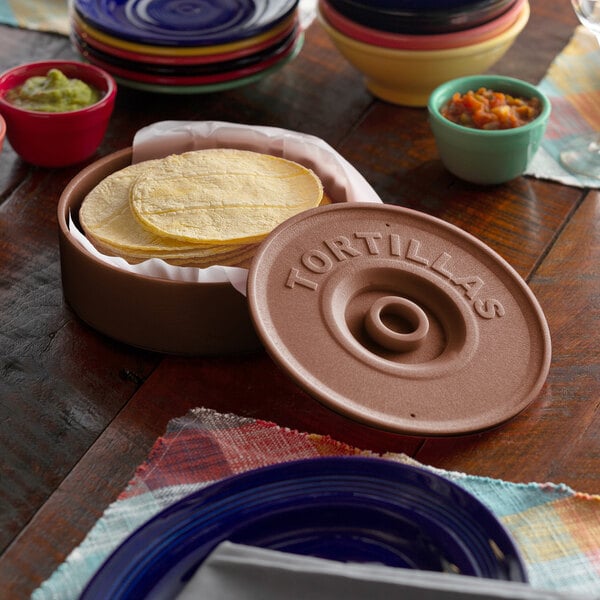 A stack of tortillas in a brown tortilla server on a table with bowls of food.