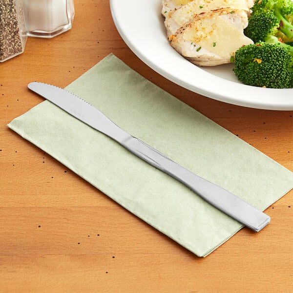 A Choice Delmont stainless steel dinner knife on a napkin next to a plate of food.