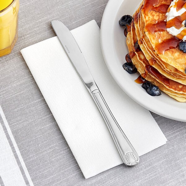 An Acopa stainless steel dinner knife on a plate of pancakes with syrup and blueberries.