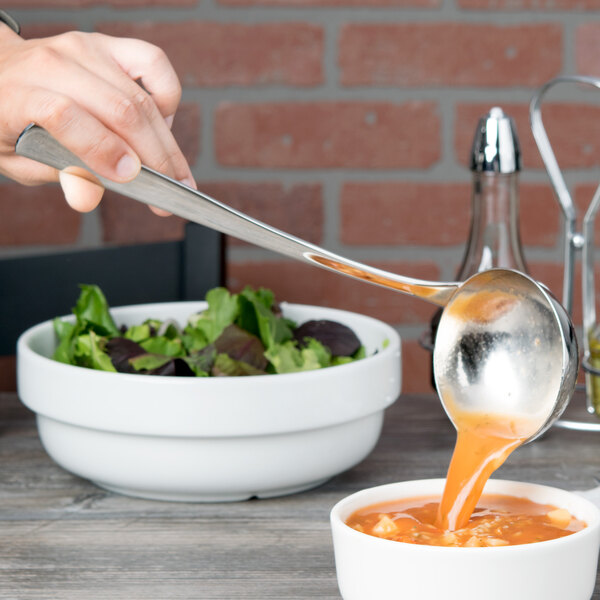 A person using an Arcoroc stainless steel soup ladle to pour soup into a bowl.