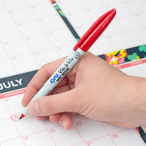 A hand using a red Expo Vis-a-Vis marker to write on a calendar.