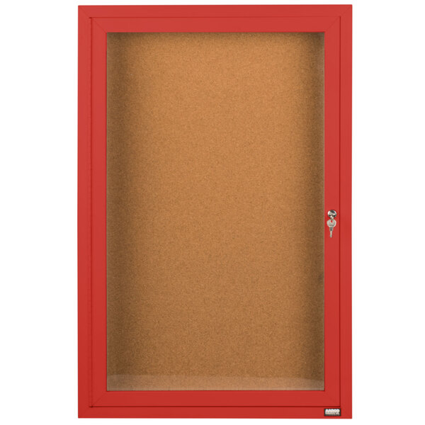A red framed Aarco bulletin board cabinet with a hinged locking door.