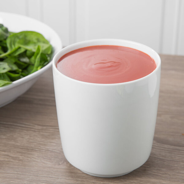 A Schonwald white dressing pot next to a bowl of spinach and a cup of red liquid.