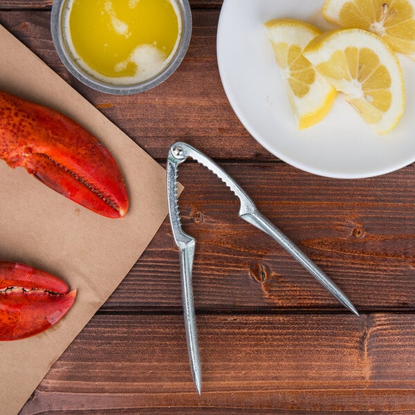 A zinc-plated steel lobster cracker cracking a lobster claw on a plate of food with lemons.