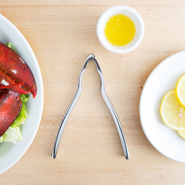 A lobster claw cracked open with a Choice stainless steel lobster cracker on a plate with lemons.