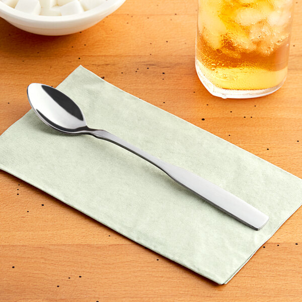 A Choice Delmont stainless steel iced tea spoon on a napkin next to a glass of ice.