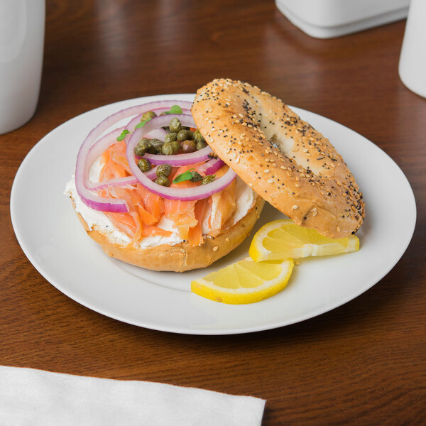 A Schonwald white porcelain plate with a bagel topped with fish, onions, and lemon.