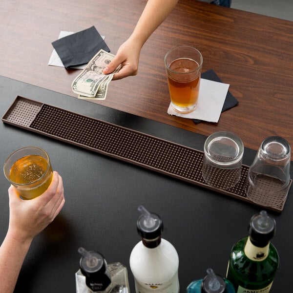 A woman holding money and a brown drink on a brown bar mat.