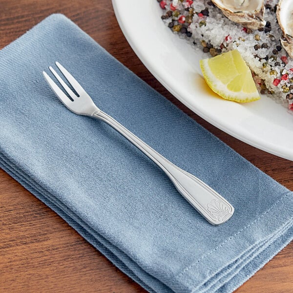 An Acopa stainless steel cocktail fork on a napkin next to a plate of lemons.
