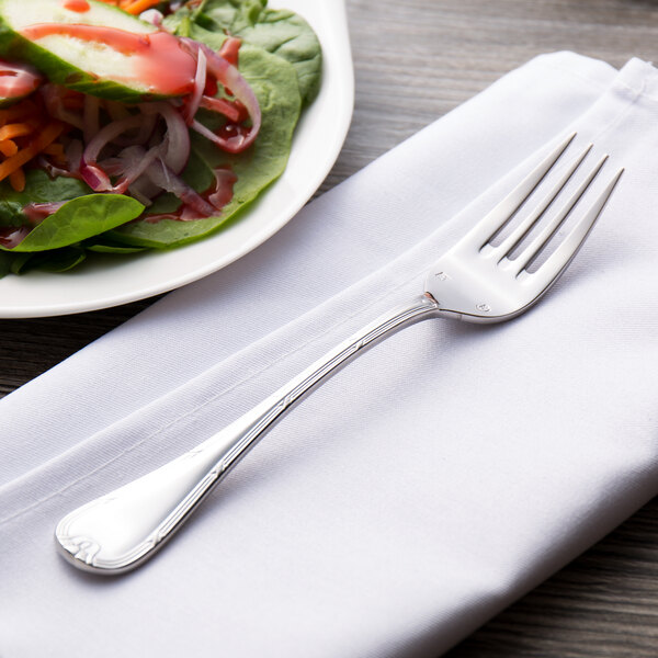 A Chef & Sommelier stainless steel salad fork on a napkin next to a plate of salad.