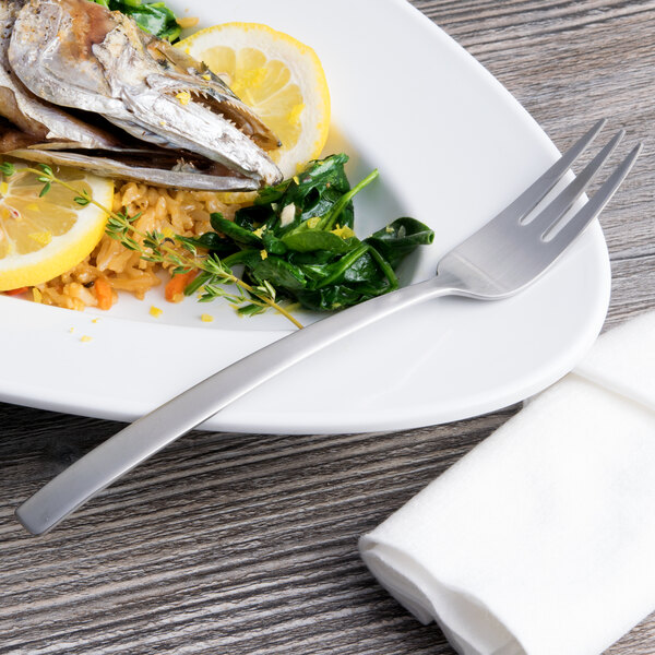 A plate of food with a fish and vegetables with an Arcoroc stainless steel fish fork on the side.