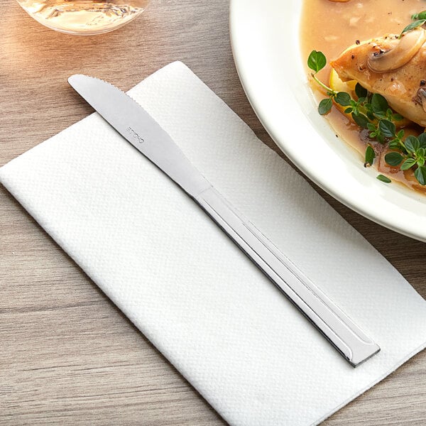 A Choice Dominion stainless steel dinner knife on a napkin next to a plate of food.