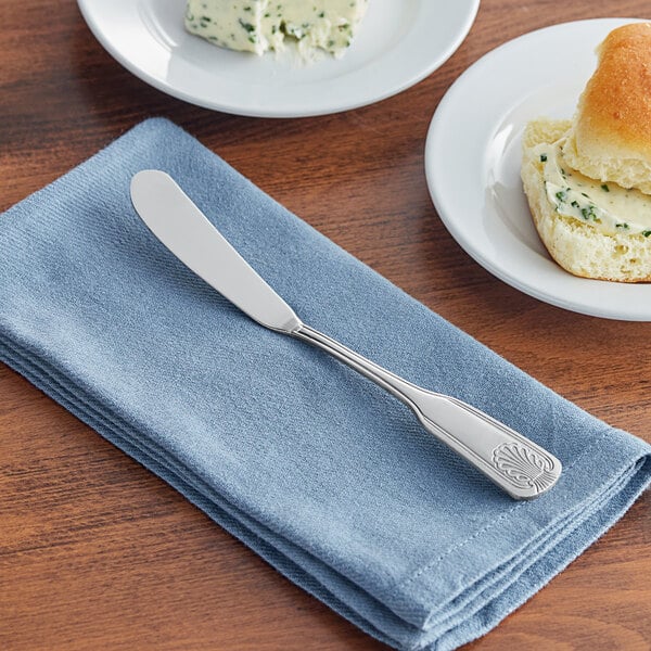 A silver Acopa butter knife on a blue napkin next to a plate of food.