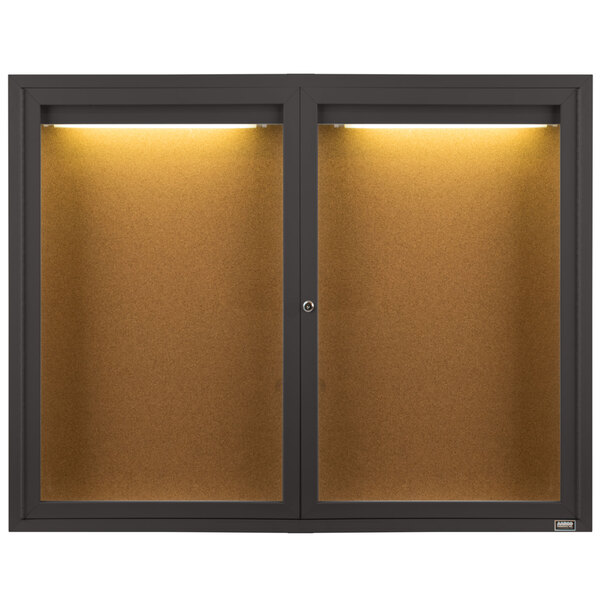 An Aarco bronze indoor lighted bulletin board cabinet with two black framed glass doors.