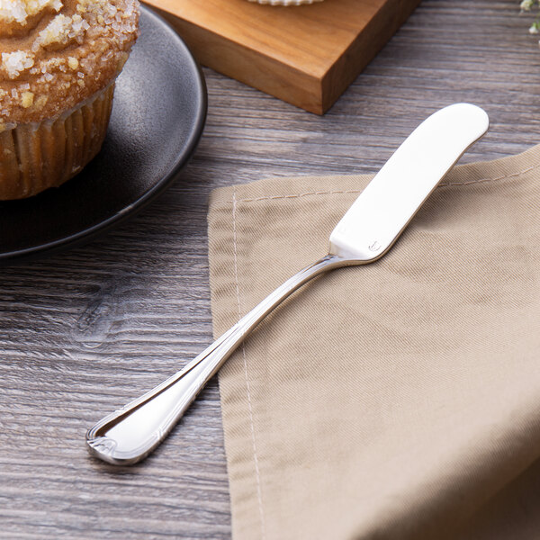 A Chef & Sommelier stainless steel butter spreader on a napkin next to a muffin.