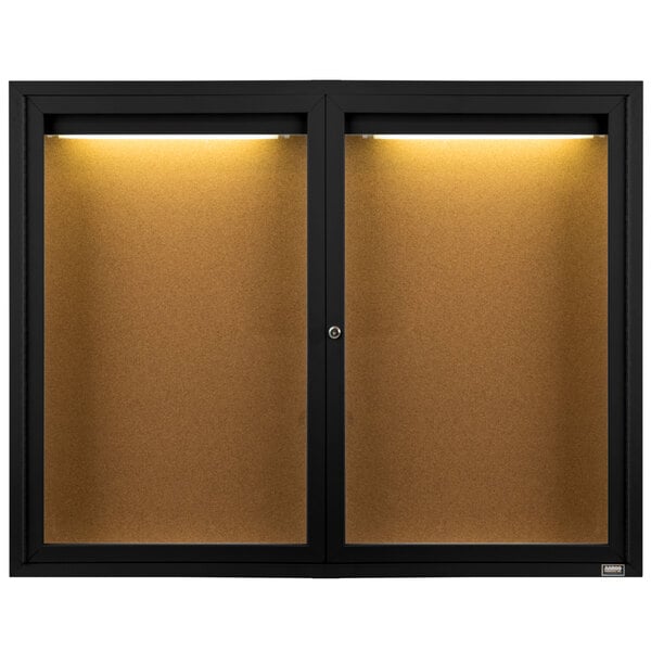 A black Aarco bulletin board cabinet with two glass doors and a light inside.