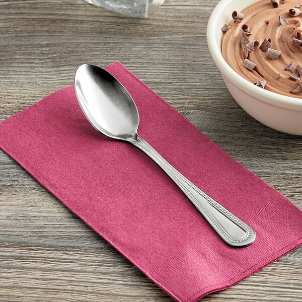A Choice Milton stainless steel teaspoon on a pink napkin next to a bowl of chocolate pudding.