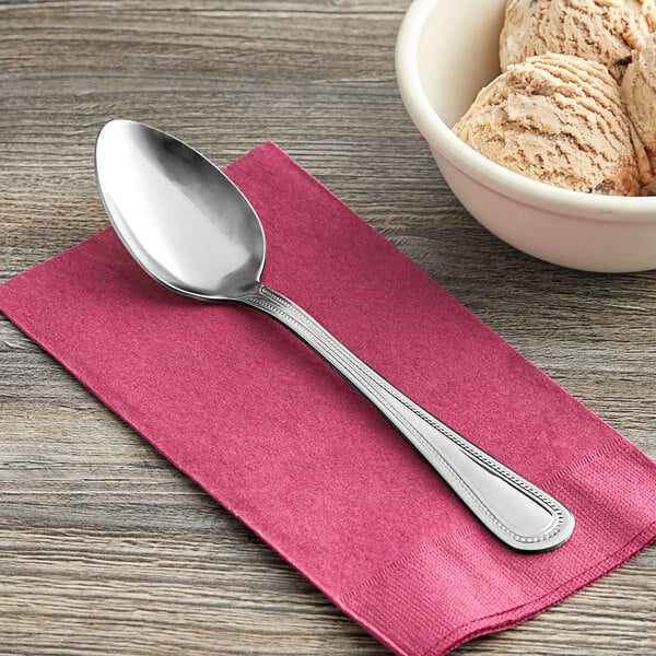 A Choice Milton stainless steel medium weight spoon on a pink napkin next to a bowl of ice cream.