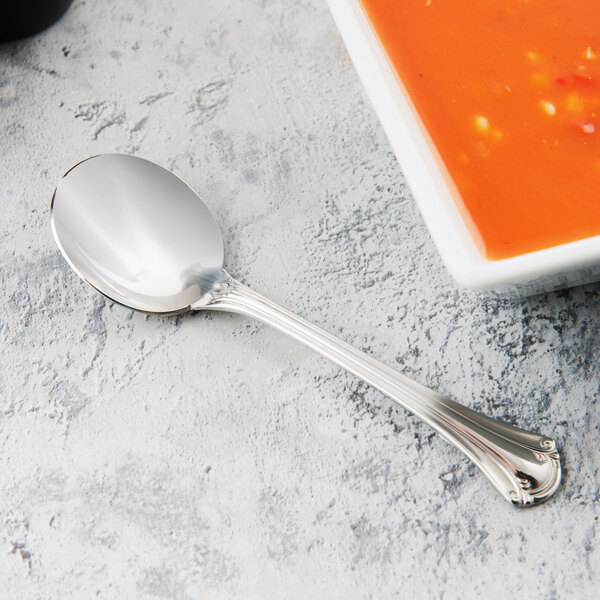 A World Tableware stainless steel bouillon spoon next to a bowl of soup.