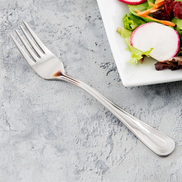 A Libbey stainless steel salad fork next to a plate of salad.