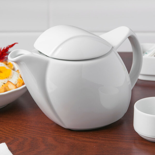 A white Schonwald Avanti Gusto teapot on a table with a bowl of fruit.