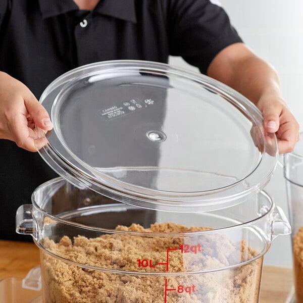 A person holding a clear lid over a clear container with brown food.