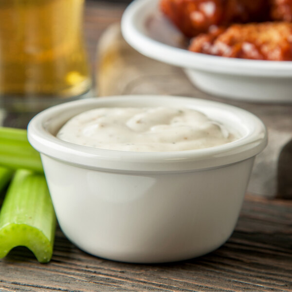 A white bowl of sauce with celery sticks in it.