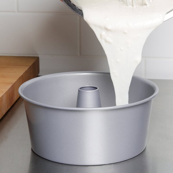 A person pouring a white liquid into a Wilton angel food cake pan.