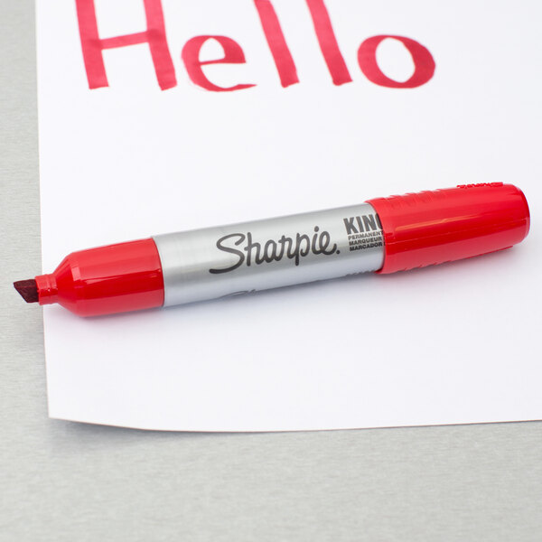 A close up of a Sharpie King Size red chisel tip marker writing the word "hello" in red on a piece of paper.