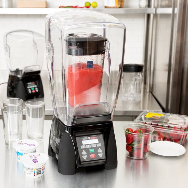 A Waring commercial blender with a plastic container full of strawberries and a glass of milk.