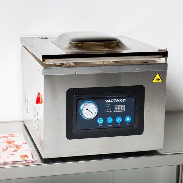 A VacPak-It chamber vacuum packaging machine on a table with a screen and a gauge.