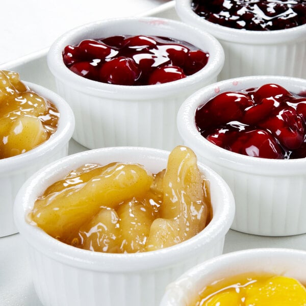 A white tray with small bowls of fruit including cherries in a Hall China bright white fluted ramekin.