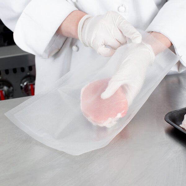 A person wearing white gloves using a VacPak-It Quart Size full mesh plastic bag to vacuum seal a piece of meat.