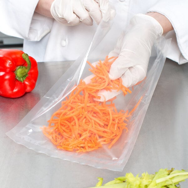 A person in white gloves using a VacPak-It chamber vacuum packaging bag to hold shredded carrots.