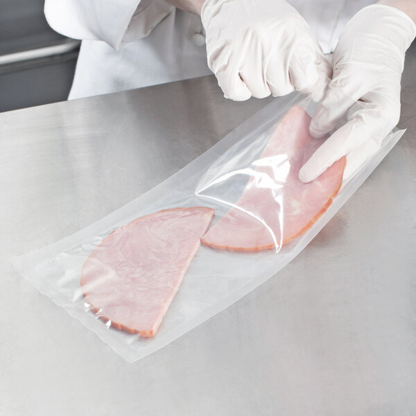 A person in gloves using a VacPak-It plastic bag to vacuum package a piece of ham.