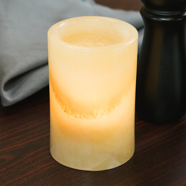A Sterno alabaster round liquid candle holder on a table with a lit candle.