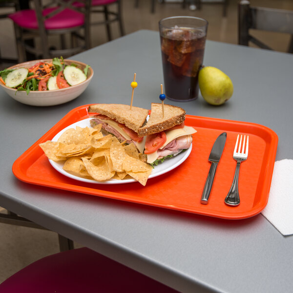 A Carlisle orange plastic fast food tray with a sandwich and chips on it.