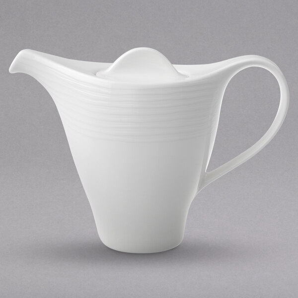 A white teapot with a handle.