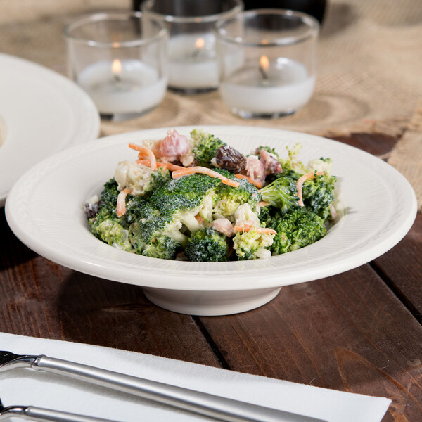 An Ivory china bowl filled with broccoli salad on a table.