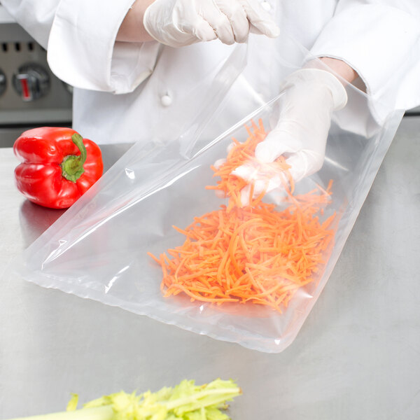A gloved hand placing shredded carrots in a VacPak-It chamber vacuum bag.
