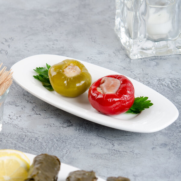 A Villeroy & Boch white porcelain oval platter with two stuffed peppers and a lemon wedge on it.