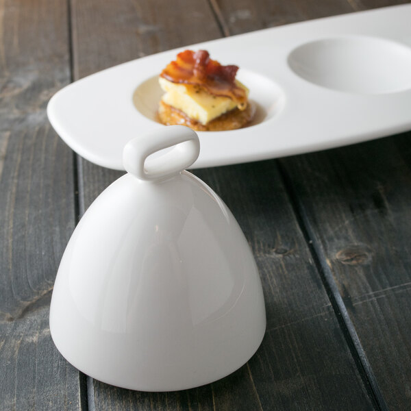 A white porcelain bell cover on a white plate with a small piece of food.