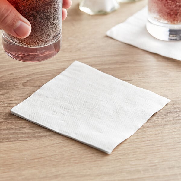 A hand using a white Choice beverage napkin to wipe a glass of liquid.