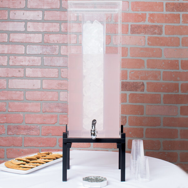 A black Cal-Mil beverage dispenser with ice in the ice chamber and a faucet on a stand.