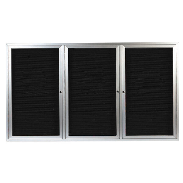 A black and silver rectangular Aarco message center with three glass doors with black metal frames.