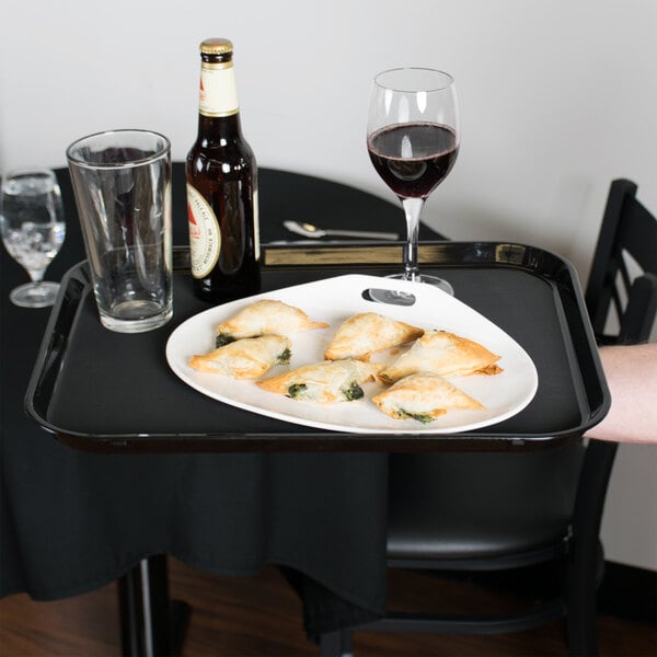 A black Cambro Polytread non-skid serving tray holding food and wine glasses on a table.