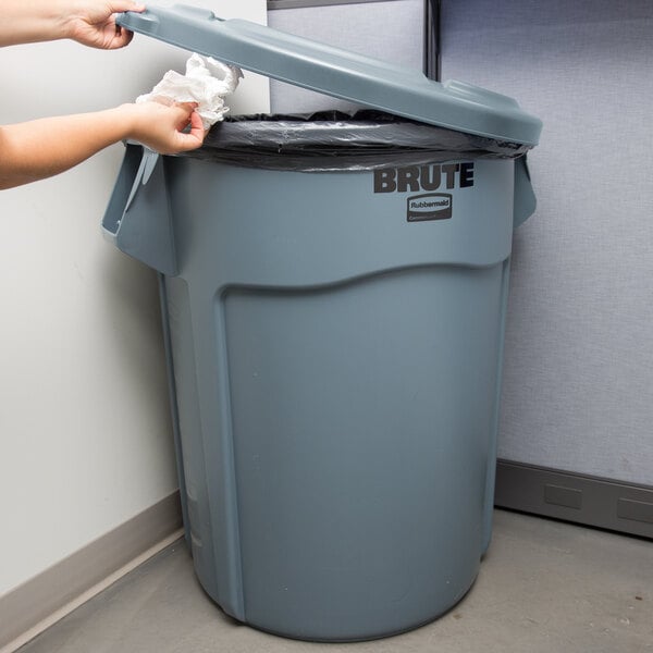 A woman putting a white cloth into a Rubbermaid BRUTE trash can in a corporate office cafeteria.