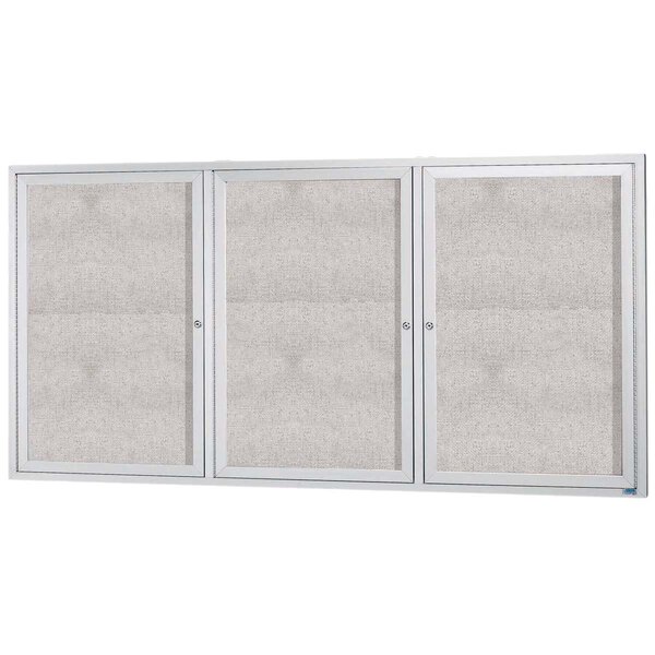 An Aarco satin anodized aluminum outdoor bulletin board cabinet with three white doors with glass panels.