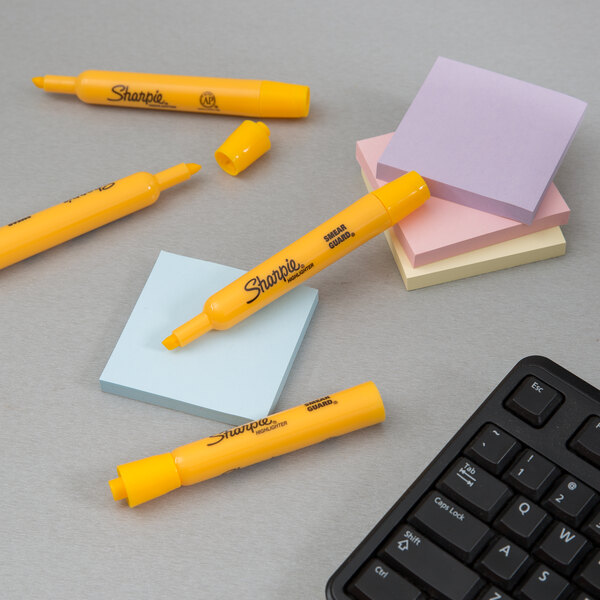 A group of Sharpie yellow tank style highlighters next to sticky notes and a keyboard.